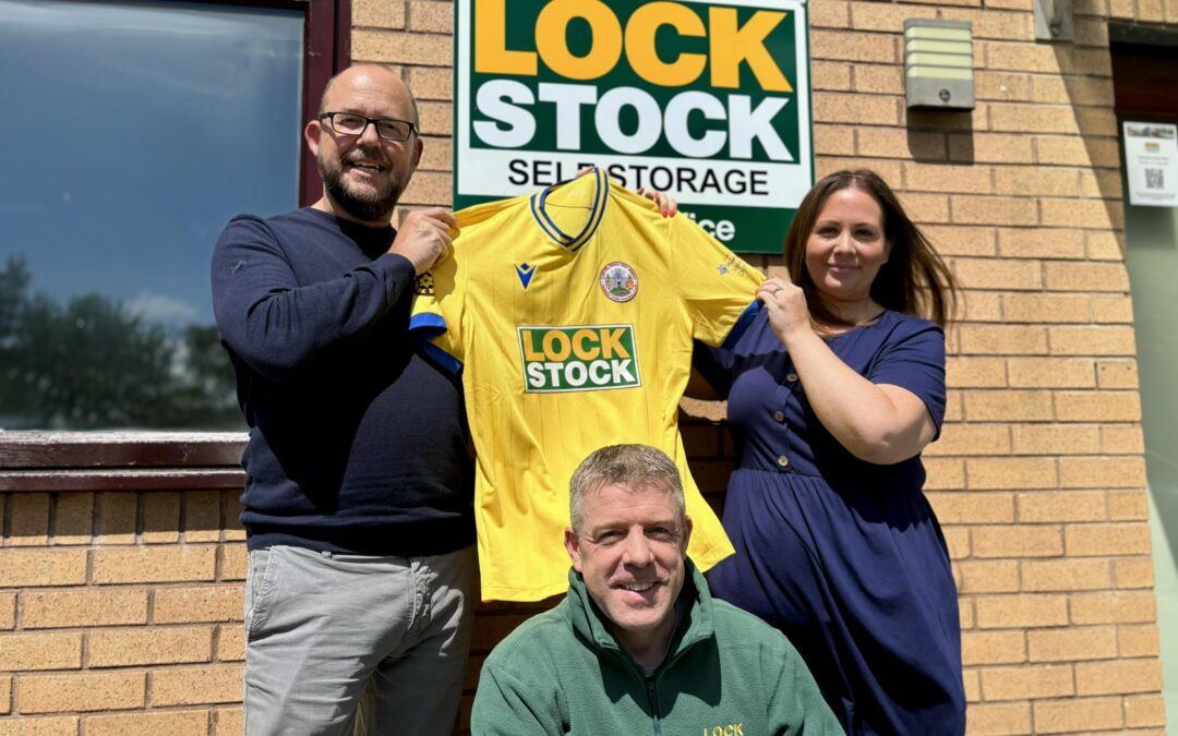 Michael Trow, Louise Catherall and Adam Jones pose with the Denbigh Town away shirt outside Lock Stock's head office.